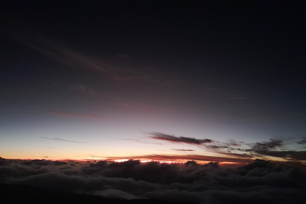 coucher de soleil nocturne à La Réunion, avec un ciel sombre et de dernières lueurs rouges au-dessus d’une mer de nuages