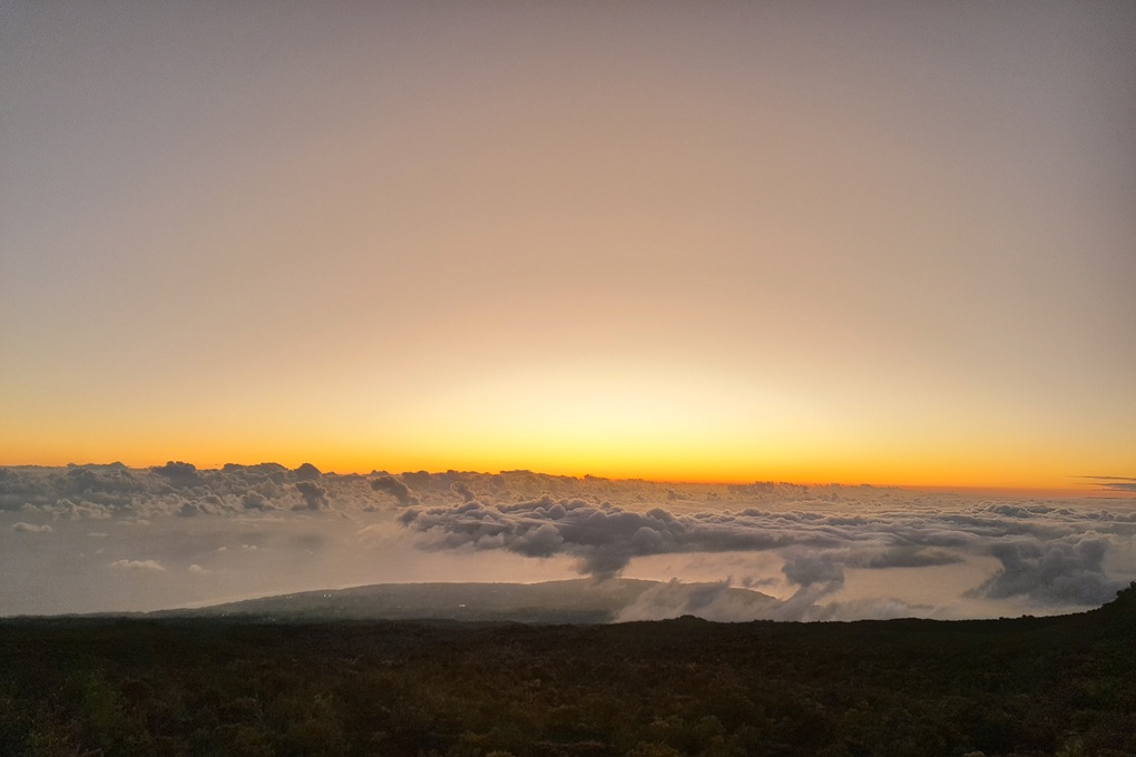 coucher de soleil à La Réunion, avec un horizon doré et des nuages bas surplombant un paysage volcanique