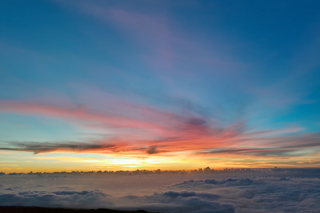 coucher de soleil coloré à La Réunion, avec un ciel bleu et rose et de fins nuages au-dessus d’une mer de nuages
