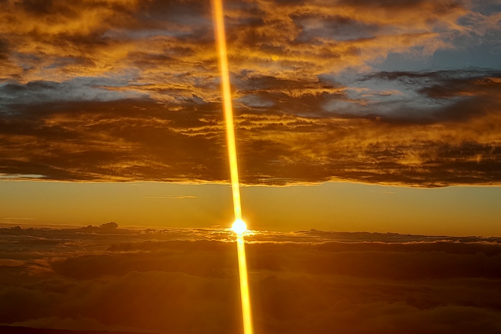 coucher de soleil spectaculaire à La Réunion, avec un rayon lumineux vertical et un ciel doré au-dessus des nuages