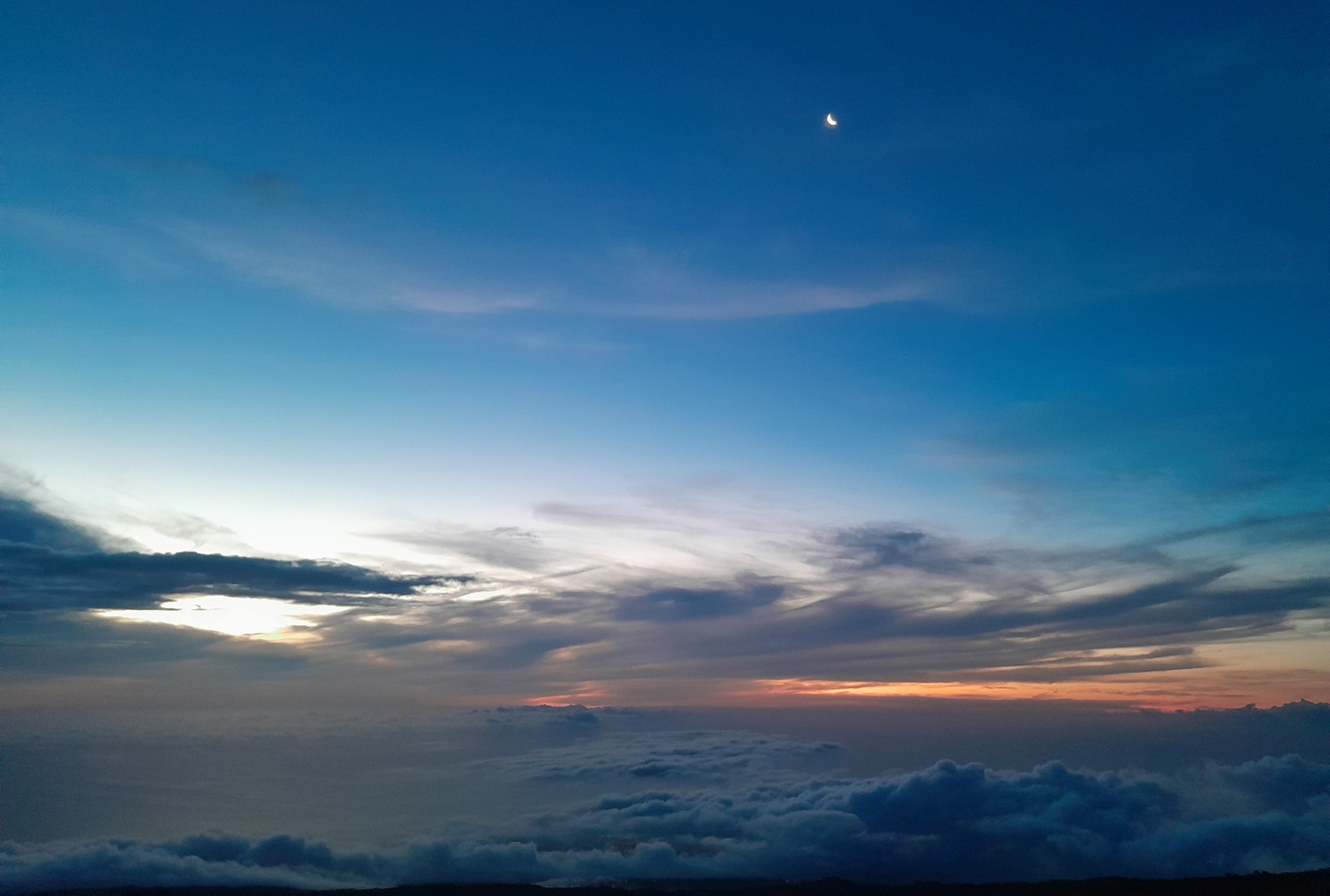 coucher de soleil à La Réunion, avec un ciel bleu profond et un croissant de lune au-dessus d’une mer de nuages