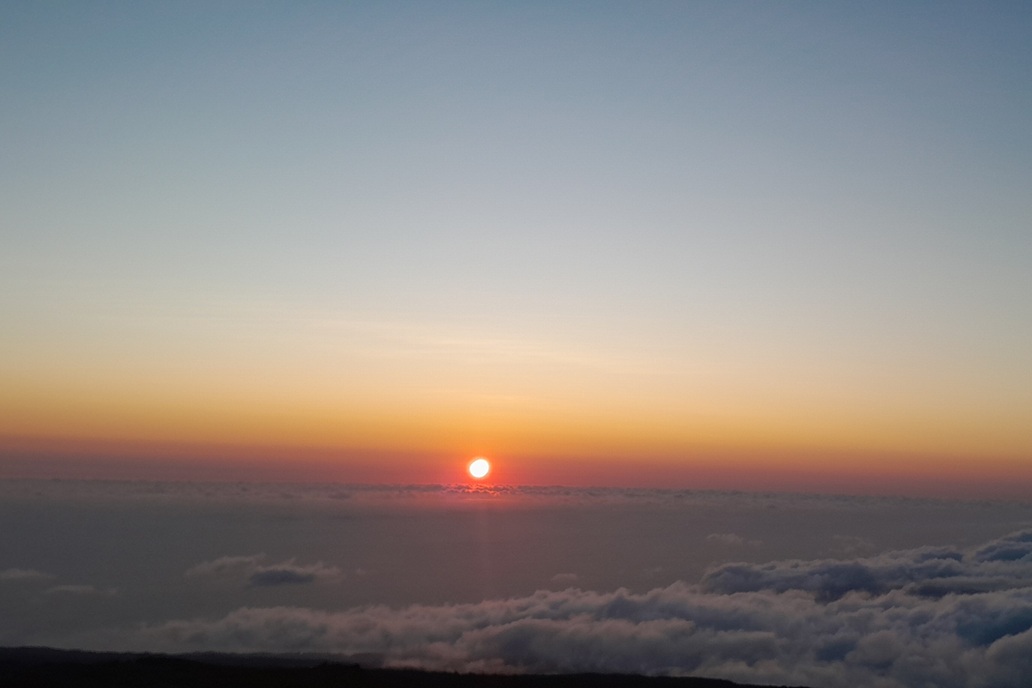 coucher de soleil à La Réunion, avec un soleil perçant les nuages et une brume colorée au-dessus de l’océan