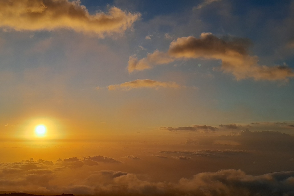 coucher de soleil lumineux à La Réunion, avec un soleil bas et un ciel doré au-dessus d’une mer de nuages