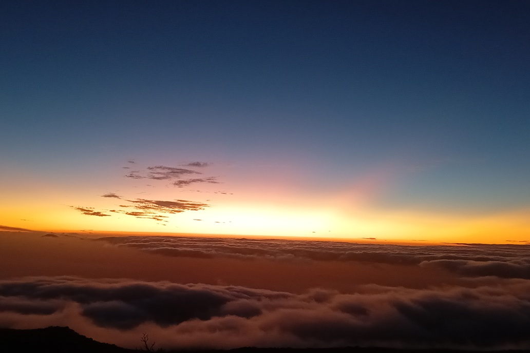 coucher de soleil à La Réunion, avec un ciel dégradé bleu et orange au-dessus d’une mer de nuages sombre