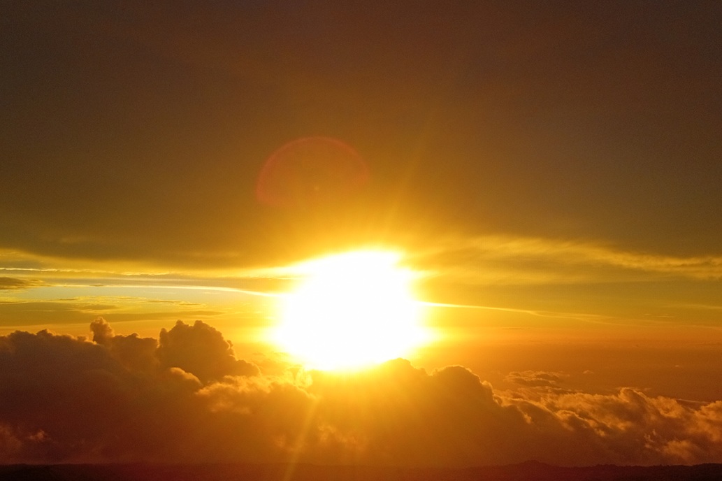coucher de soleil lumineux à La Réunion, avec le soleil couchant sur une mer de nuages et un ciel orange profond