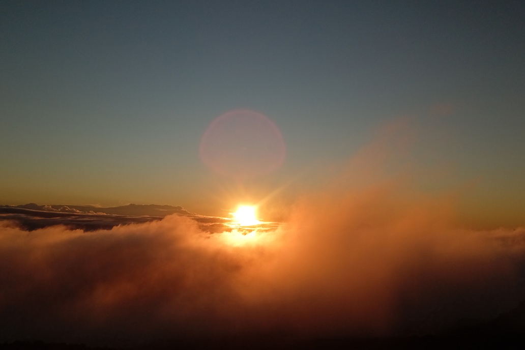 coucher de soleil lumineux à La Réunion, avec un soleil perçant les nuages et une brume dorée au-dessus du relief