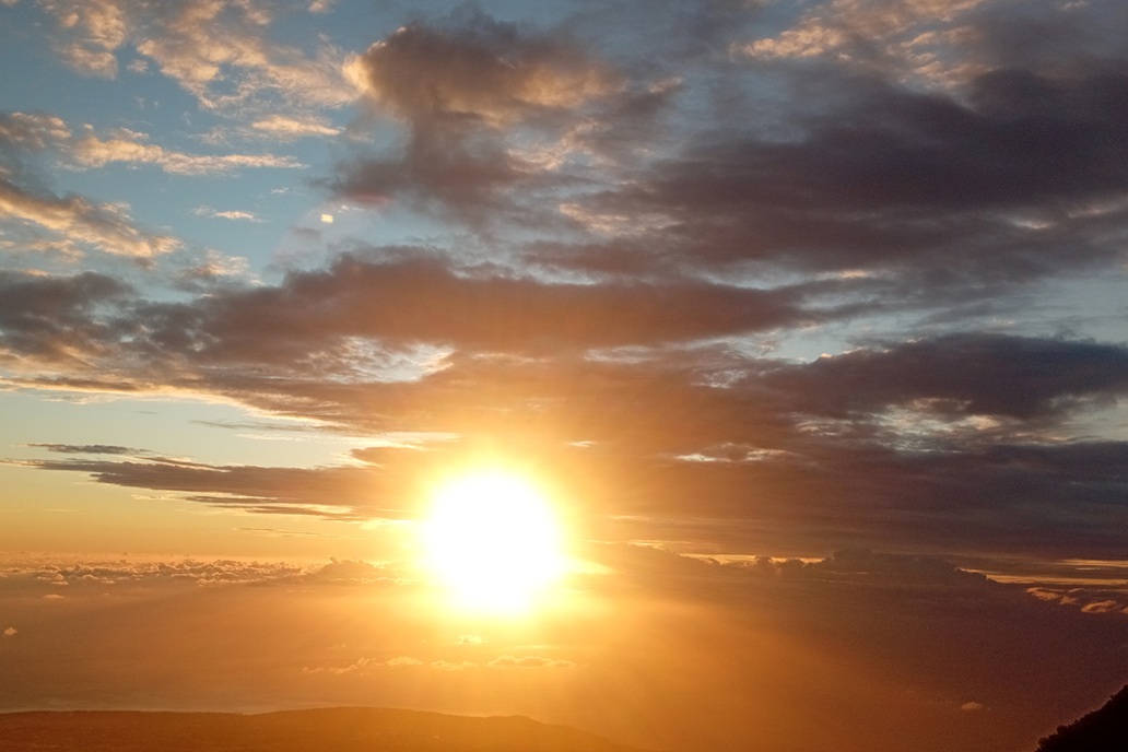 coucher de soleil lumineux à La Réunion, avec un soleil rayonnant entre les nuages et un ciel partiellement couvert